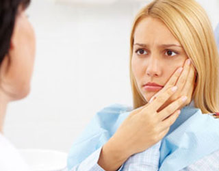 Woman looking at dentist holding cheek in pain.